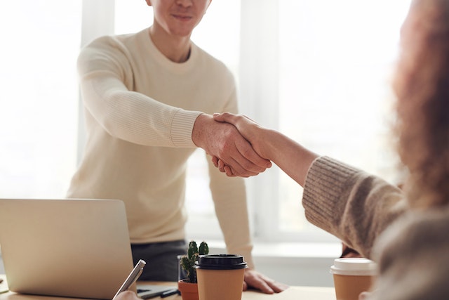 two people shaking hands in front of laptop